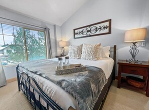Un dormitorio con cama, mesitas de noche, una ventana con persianas y un elemento decorativo en la pared.