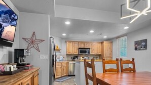 A modern kitchen with wooden cabinets, a dining table, and a TV mounted on the wall. - Mountain Panda Paradise, 2BR Redstone Townhome, Close to Canyons (Park City)