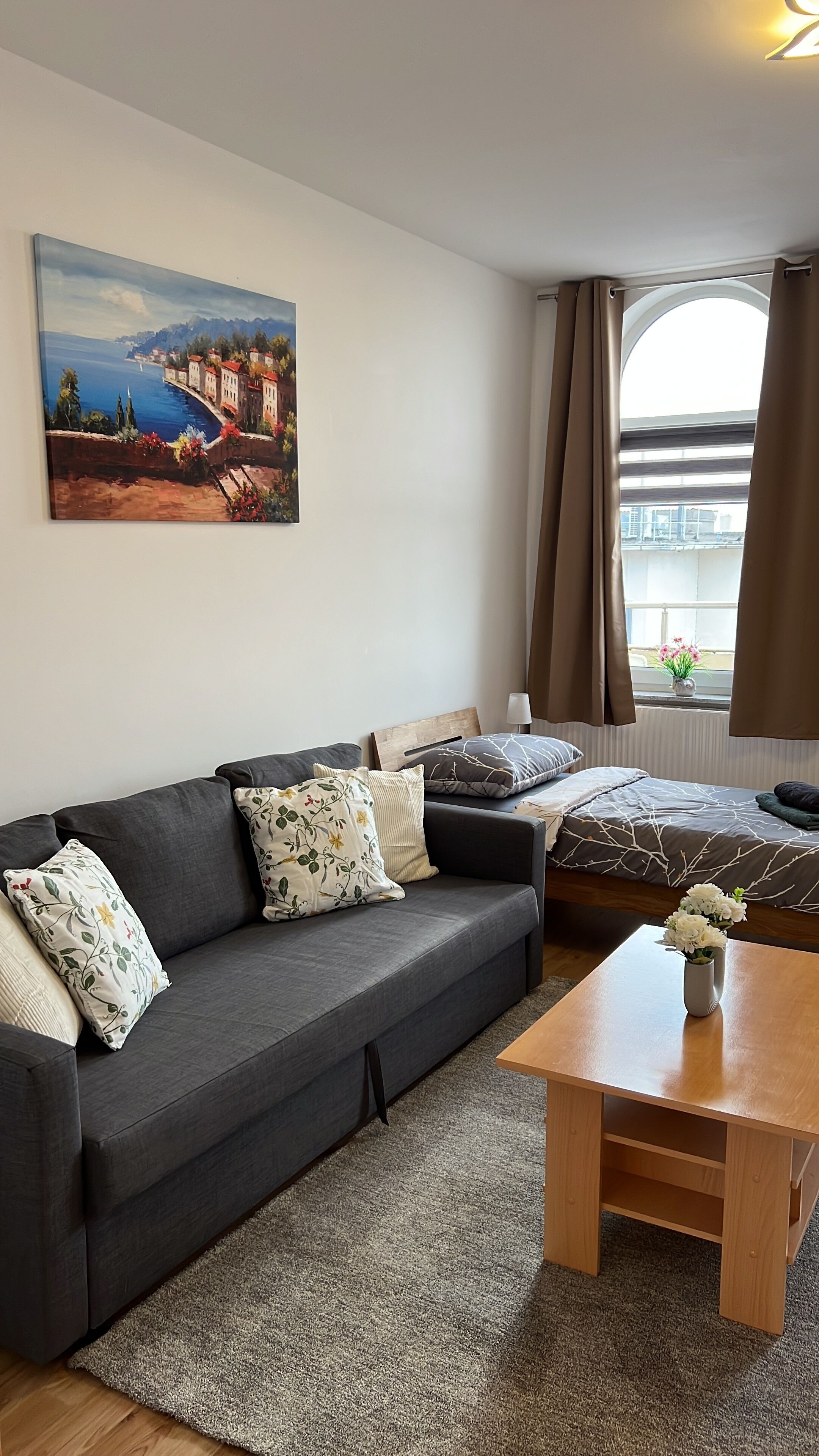 Ein modernes Wohnzimmer mit einem dunkelgrauen Sofa, einem Holztisch und einem Gemälde einer Küstenlandschaft an der Wand.