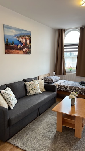 A modern living room with a dark grey sofa, a wooden coffee table, and a painting of a coastal scene on the wall. - Blunest Apartment 4: 4-Bedroom Apartment with Parking Space and Balcony (Bremerhaven)