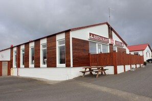 A two-story building with a sign indicating it is a restaurant and hotel. There is a wooden fence in front, and a picnic table is visible. - Relaxing and family-friendly hotel by the ring road yet surrounded by nature (Akranes)