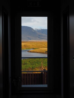 A door leading to a room with a view of a mountainous landscape and a body of water. - Relaxing and family-friendly hotel by the ring road yet surrounded by nature (Akranes)