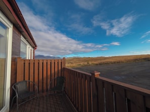 A wooden deck with two chairs, a view of a flat landscape, and a clear sky. - Relaxing and family-friendly hotel by the ring road yet surrounded by nature (Akranes)