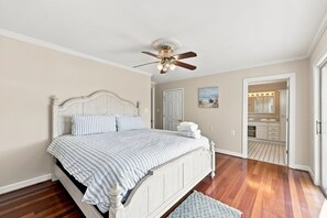 Ein Schlafzimmer mit Bett, Deckenventilator, einer Tür und einem durchgehenden Türspalt sichtbaren Badezimmer.