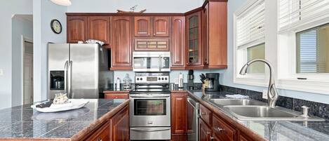 Una cocina con armarios de madera, electrodomésticos de acero inoxidable, encimera de granito y una ventana con persianas.