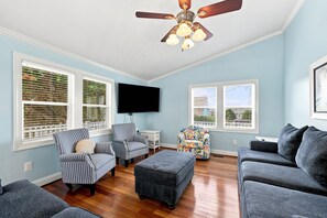A living room with a ceiling fan, two windows with blinds, a flat-screen TV, and a couch. - Rest Coast Repeat-Just a short walk to the beach! (Atlantic Beach)