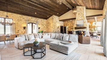 A spacious living room with a stone wall, a large sofa, a fireplace, and a dining area.