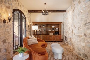 Une pièce chaleureuse avec un mur en pierre, un meuble en bois, un fauteuil marron et une petite table ronde agrémentée d’une plante.