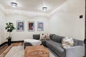 A modern living room with a grey sectional sofa, a brown leather ottoman, and framed posters on the wall. - New! Stone Castle Estate in Roxborough State Park (Littleton)