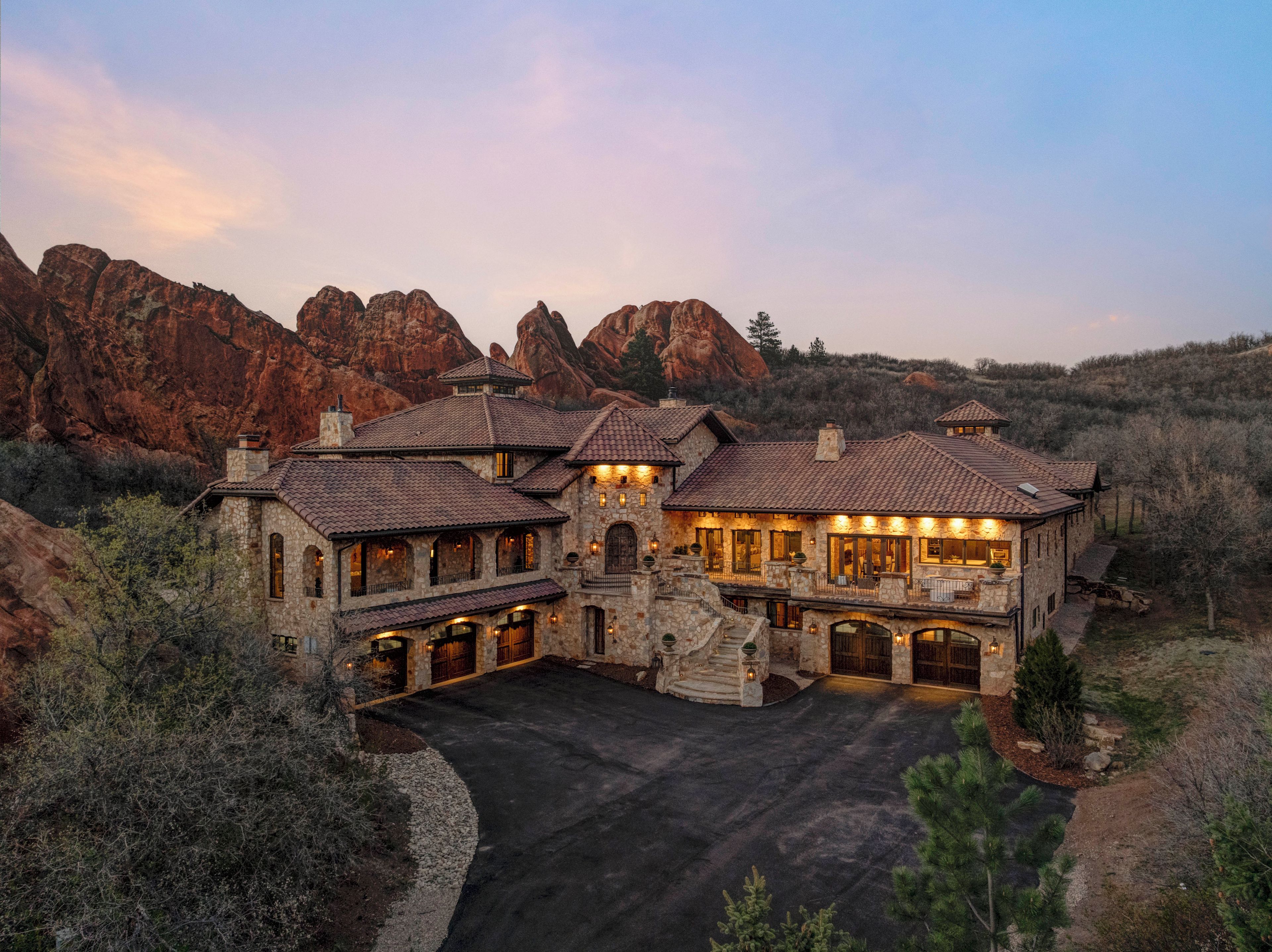A large, multi-story stone building with a spacious driveway and a mountain backdrop.