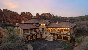 A large, multi-story stone building with a spacious driveway and a mountain backdrop.