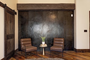 A room with a large wooden door, two leather chairs, a small table with a plant, and a wooden floor.
