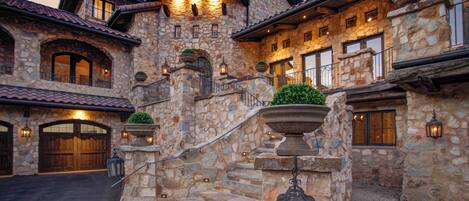 A stone building with a grand staircase, multiple windows, and outdoor lighting fixtures.