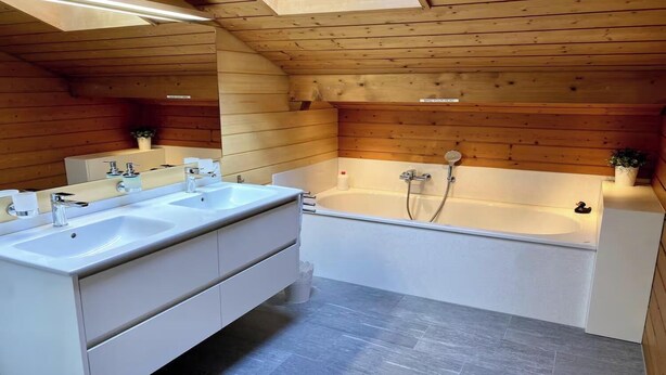 Ein modernes Badezimmer mit einem Doppelwaschtisch, einer Badewanne und einem Oberlicht.