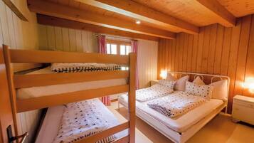 A wooden cabin bedroom with bunk beds and a single bed, a nightstand, and a window with curtains.