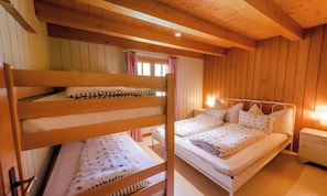 A wooden cabin bedroom with bunk beds and a single bed, a nightstand, and a window with curtains.