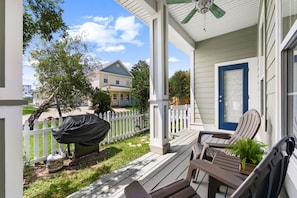 A covered porch with outdoor furniture, a white picket fence, and a house in the background. - Paradise Escape | 3BR Beach Home in Crystal Beach (Destin)