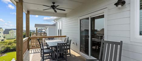 Un patio exterior techado con mesa y sillas, un ventilador de techo y vistas a casas vecinas.