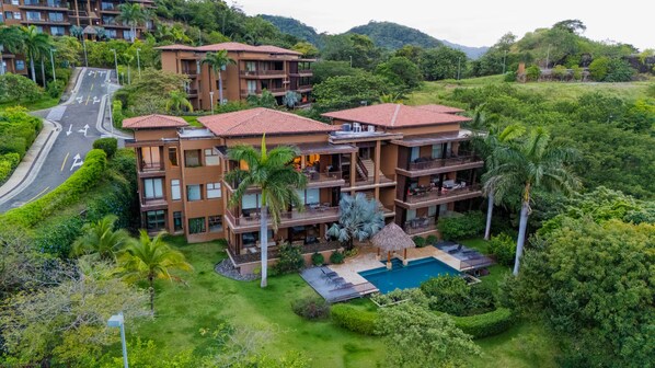 Un hotel su più piani con piscina, immerso nel verde e affiancato da una strada.
