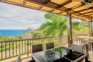 A covered outdoor area with a table and chairs, overlooking a scenic view of the ocean and lush greenery. - New Listing • Azul Paraiso • 3BR Condo • Ocean Views (Sardinal)