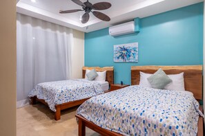 A hotel room with two beds, a ceiling fan, an air conditioning unit, and a painting on the wall. - New Listing • Azul Paraiso • 3BR Condo • Ocean Views (Sardinal)