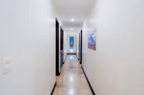 A hallway with doors on both sides, a light switch on the left, and a painting on the right. - New Listing • Azul Paraiso • 3BR Condo • Ocean Views (Sardinal)