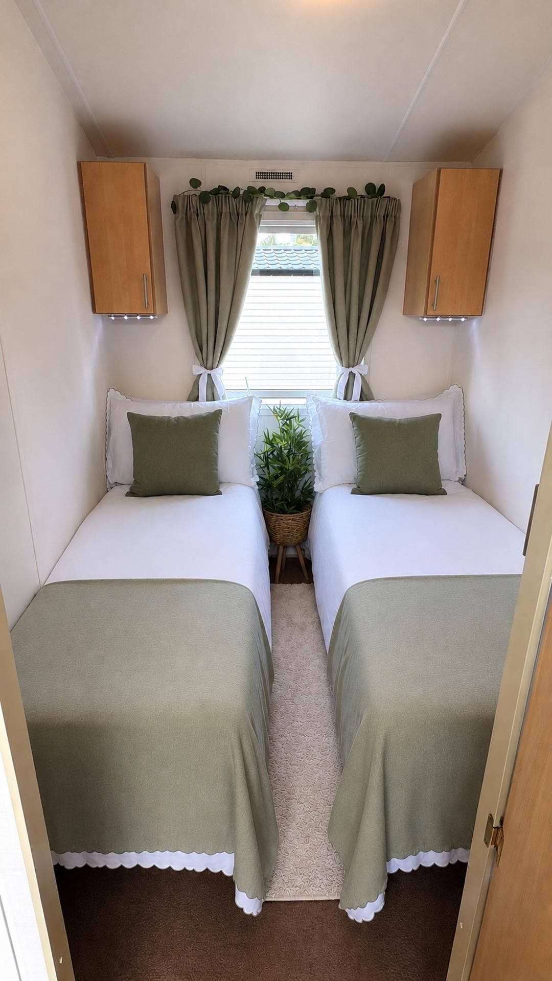 Interior compacto de autocaravana con dos camas, una mesita con una planta y armarios superiores.