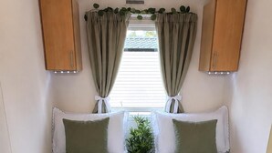 A compact RV interior with two beds, a small table with a plant, and overhead cabinets.
