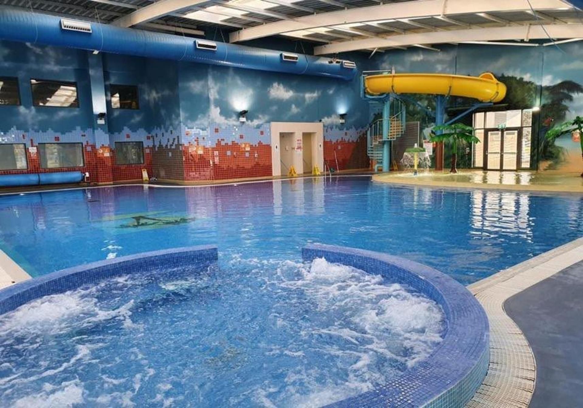 Una piscina interior con hidromasaje, un tobogán de agua y un mural en las paredes.