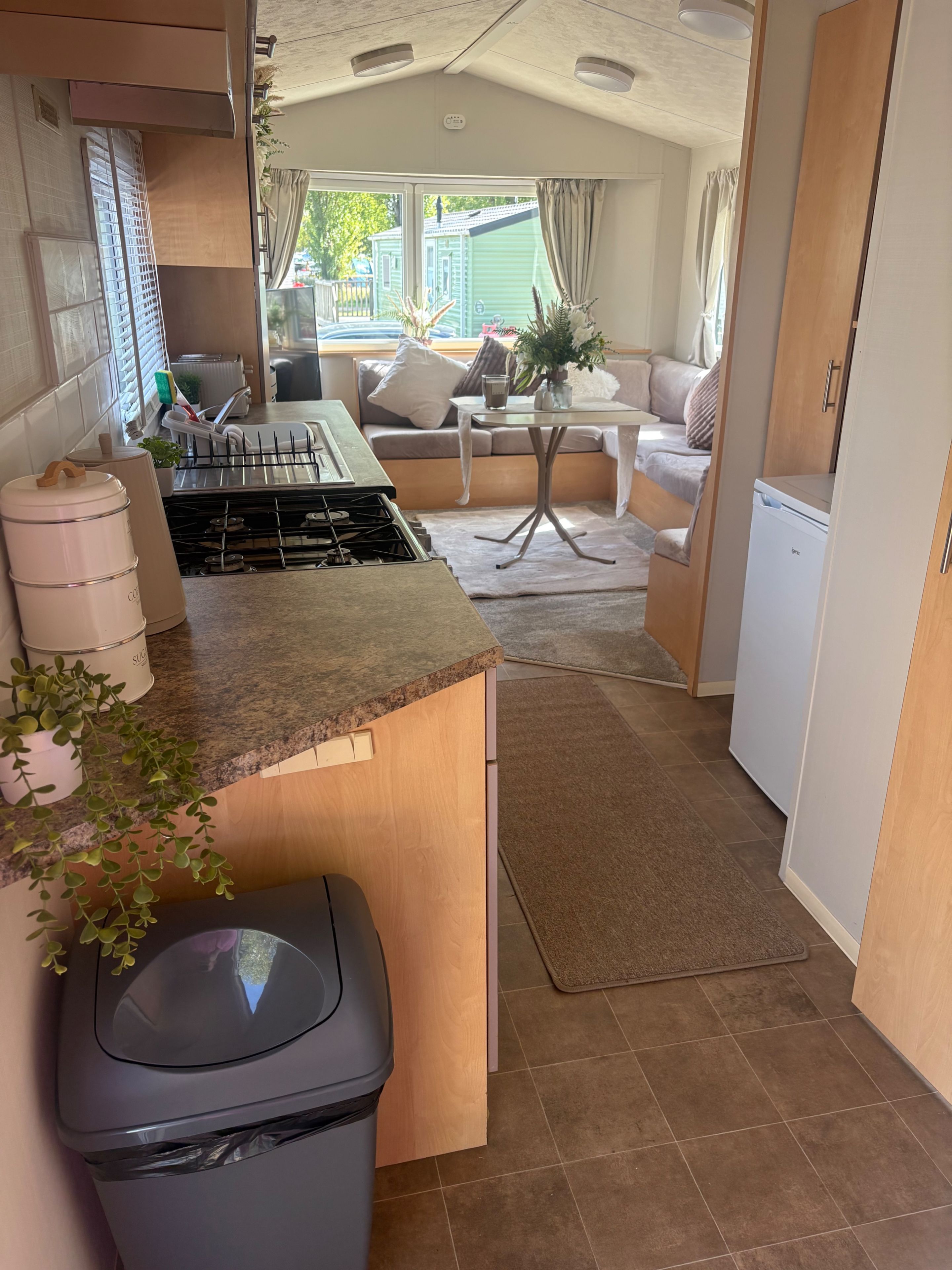 Cocina compacta con estufa a gas, un bote de basura y un pequeño comedor con mesa y sillas.