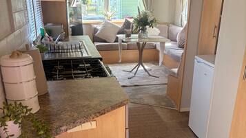 Cocina compacta con estufa a gas, un bote de basura y un pequeño comedor con mesa y sillas.