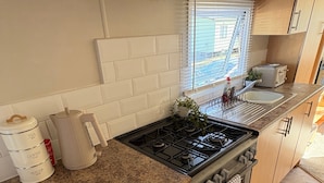 A compact kitchen with a gas stove, a sink, and a window with blinds.
