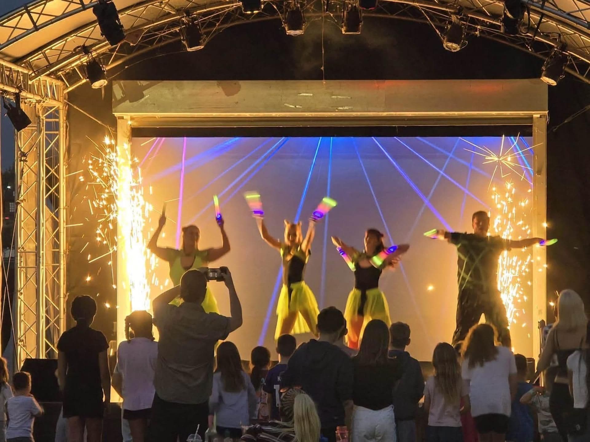 A stage with a crowd of people, some holding up light sticks.