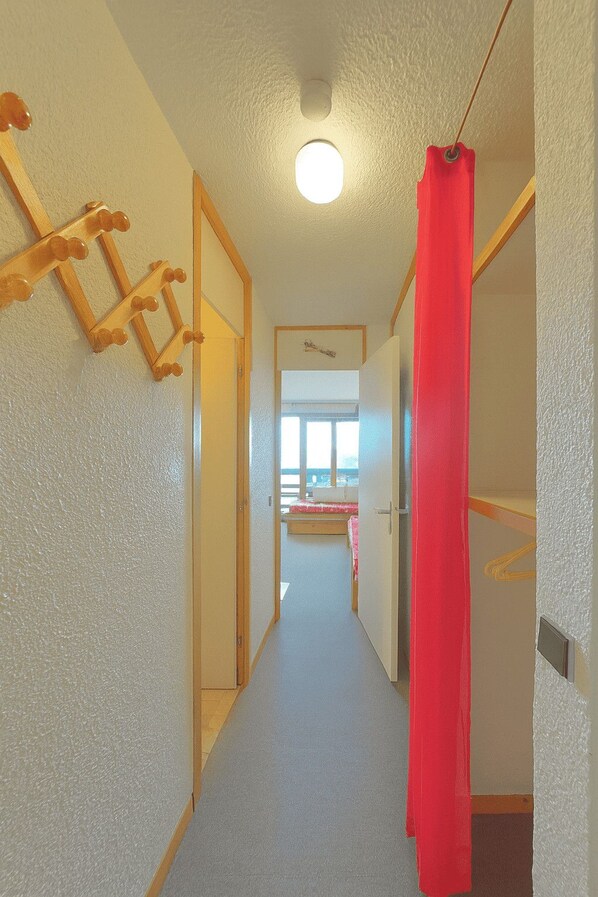 A narrow hallway with a wooden ladder on the left, a red curtain on the right, and a door at the end leading to a room with a window. - Cozy apartment near the ski slopes (Les Allues)