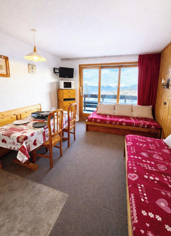 Ein Zimmer mit Esstisch, Stühlen, einer Couch, einem Fernseher und einem Fenster mit Blick.