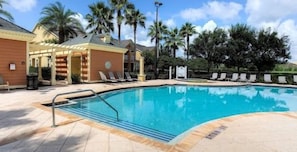 A swimming pool with lounge chairs, a covered seating area, and palm trees in the background. - 5BR Pool & Spa Home with Themed Rooms 376 (KISSIMMEE)