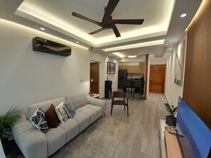 A modern living room with a sofa, a ceiling fan, recessed lighting, and a kitchen in the background. - Modern and cozy 2-bedroom apartment with AC in the university area Santo Domingo (Santo Domingo)