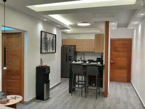 A compact kitchen with wooden cabinets, a refrigerator, a sink, and a dining area with two chairs. - Modern and cozy 2-bedroom apartment with AC in the university area Santo Domingo (Santo Domingo)