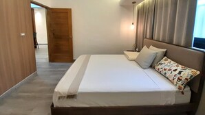 Ein Schlafzimmer mit einem Bett, einem Nachttisch, einer Lampe, einem Fenster mit Vorhängen und einer Tür zu einem anderen Raum.
