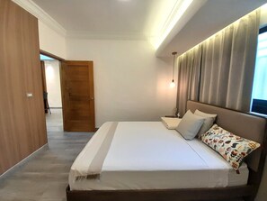 A bedroom with a bed, a nightstand, a lamp, a window with curtains, and a door leading to another room. - Modern and cozy 2-bedroom apartment with AC in the university area Santo Domingo (Santo Domingo)