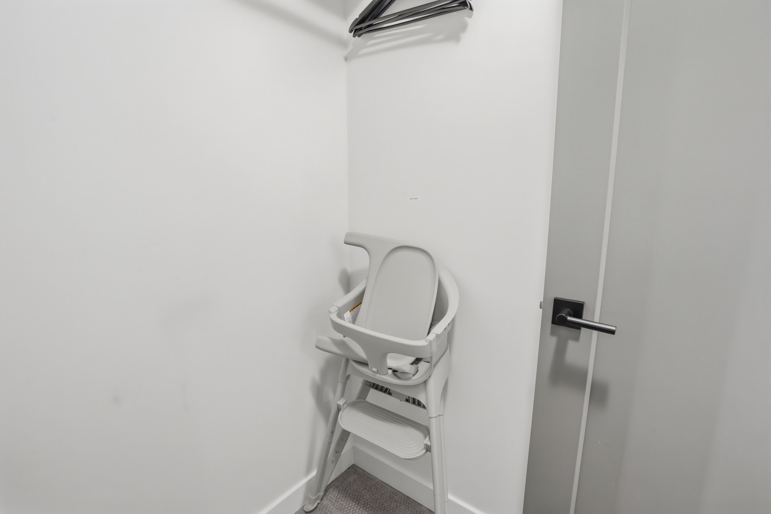 A white door with a silver handle and a white chair with a tray in a corner.
