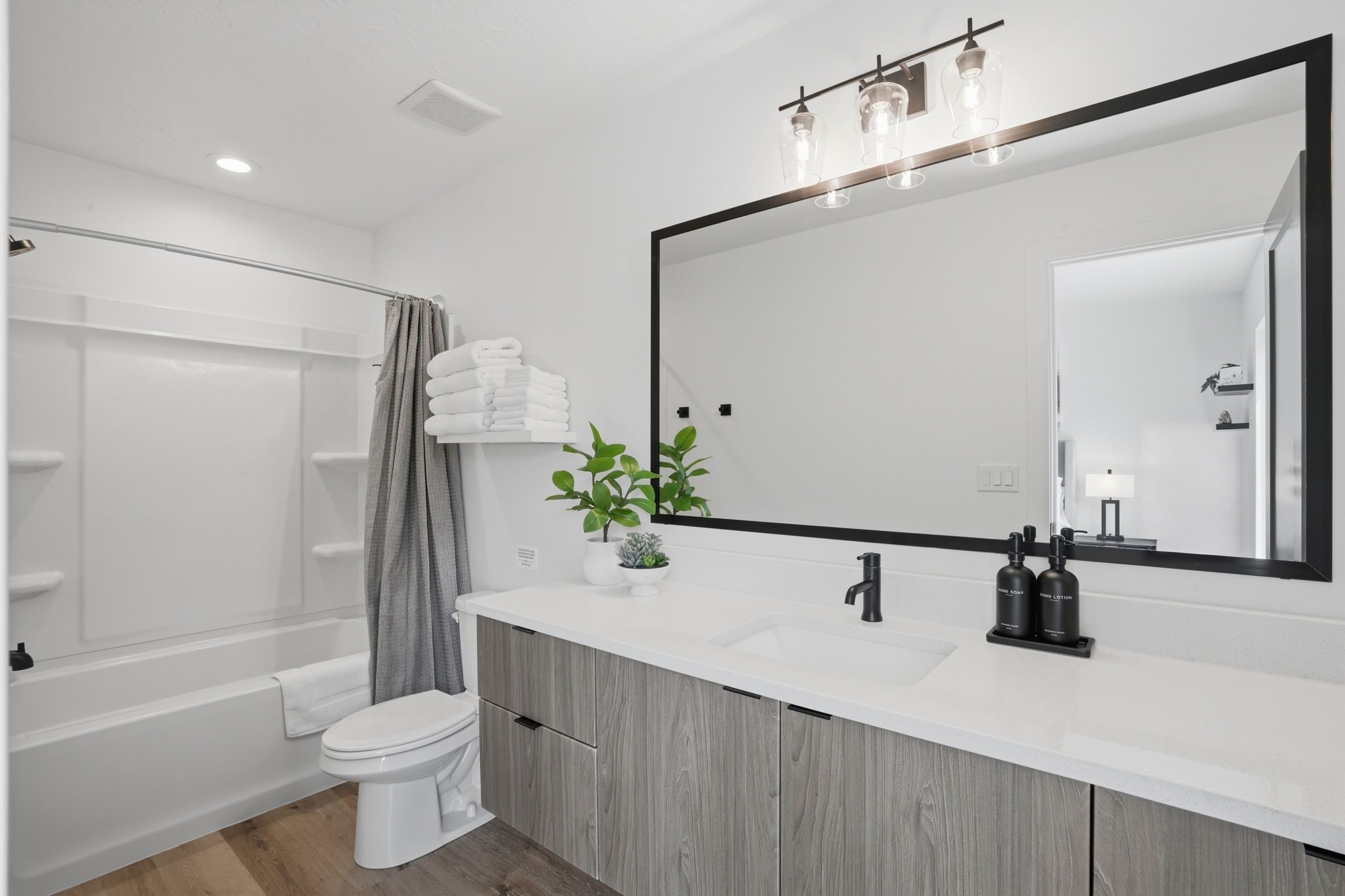 A modern bathroom with a white vanity, a large mirror, and a shower area.