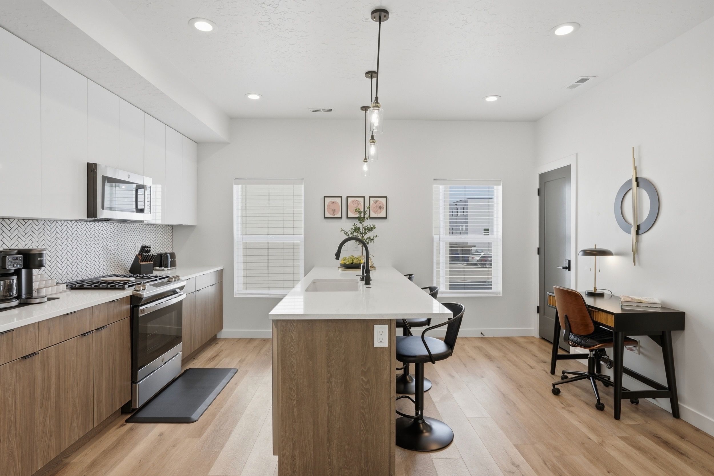 A modern kitchen with a central island, built-in appliances, and a dining area with a desk and chairs.