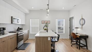 A modern kitchen with a central island, built-in appliances, and a dining area with a desk and chairs.