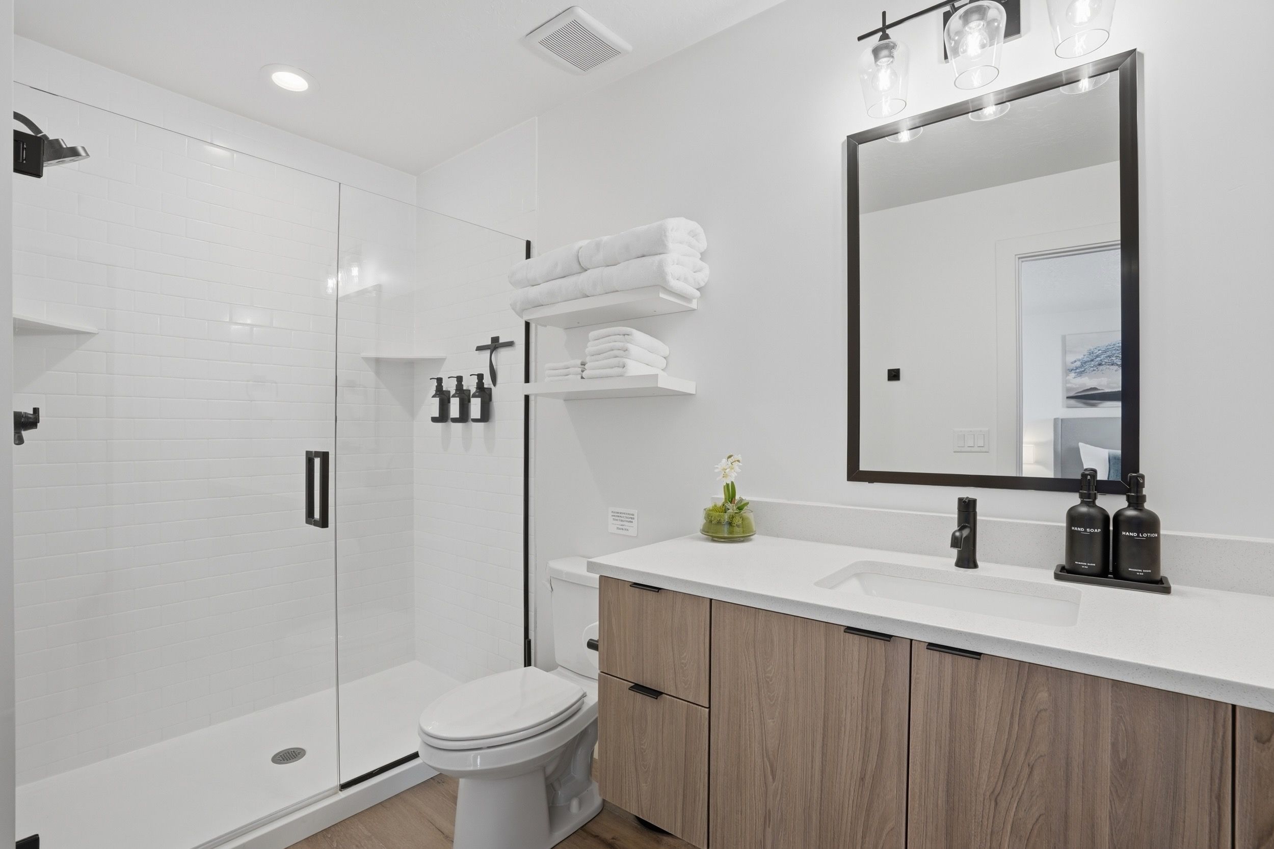 Un baño moderno con cabina de ducha de vidrio, inodoro, tocador con espejo y lavamanos.