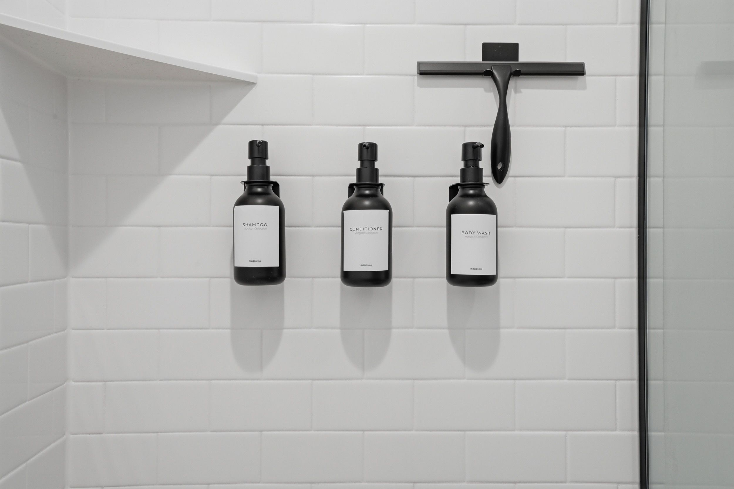 Ein Badezimmer mit drei Flaschen Shampoo, Conditioner und Duschgel an einer weißen, gefliesten Wand.