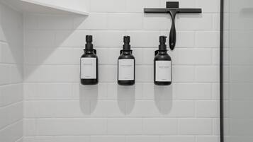 Ein Badezimmer mit drei Flaschen Shampoo, Conditioner und Duschgel an einer weißen, gefliesten Wand.