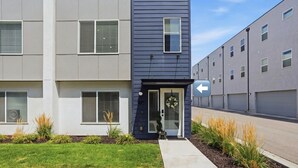 Un immeuble d’appartements moderne, avec une façade grise, un petit jardin devant et une porte ornée d’une guirlande.