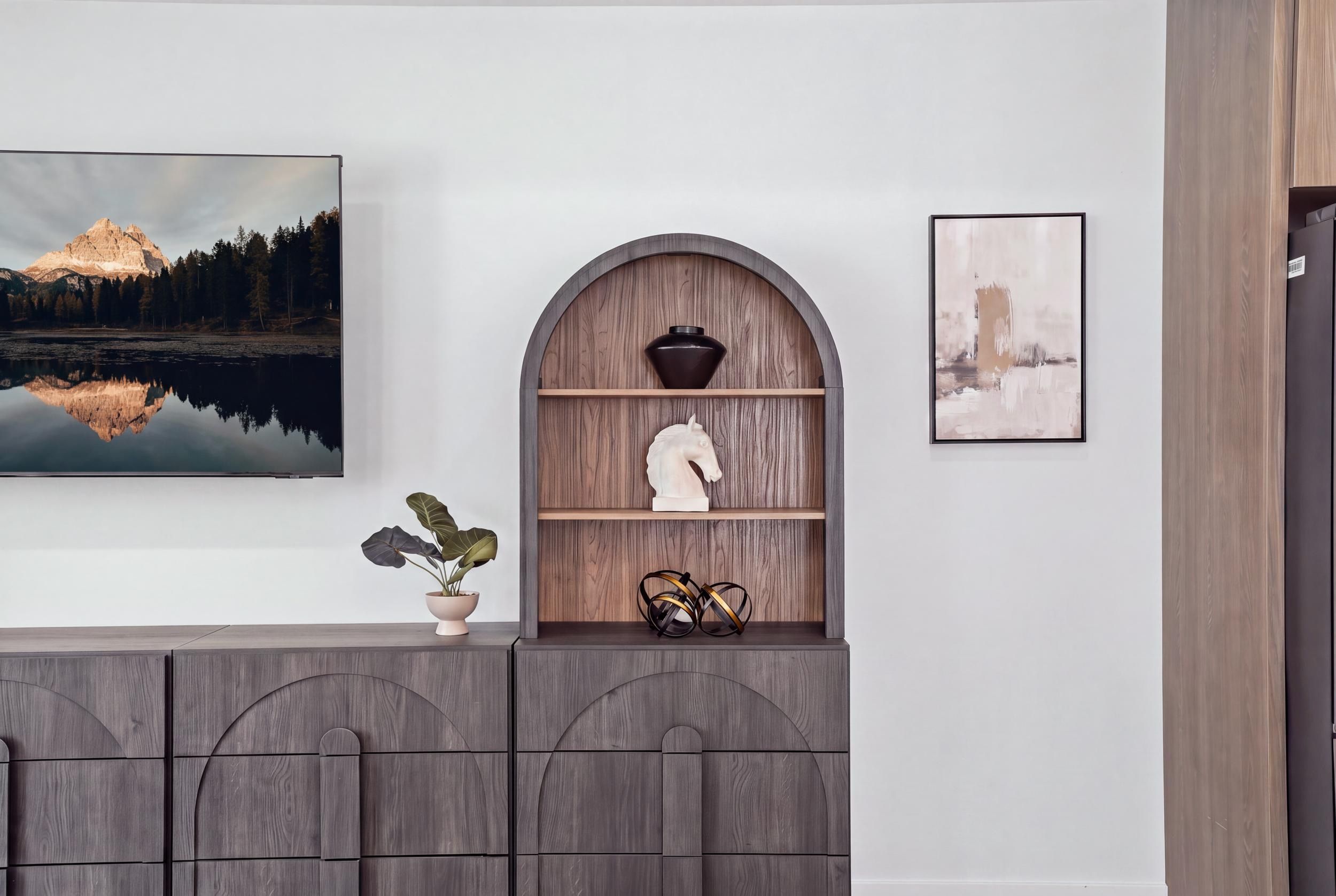 A room with a large painting of a mountain landscape, a shelf with decorative items, and a framed picture on the wall.