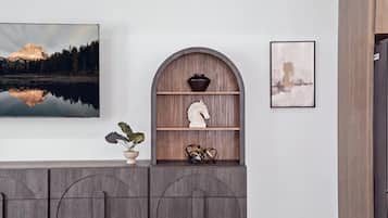 A room with a large painting of a mountain landscape, a shelf with decorative items, and a framed picture on the wall.